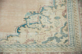 Distressed Oushak rug spandrel with textured ivory field, ocean green, and pale chestnut motifs.
