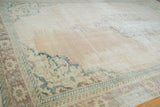 Distressed Oushak rug corner showing faded cream, pale chestnut, and deep green motifs.