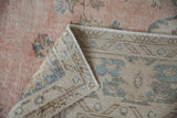 Distressed Sparta carpet corner, showing dusty blush pile, and reverse with pale blue geometric patterns.