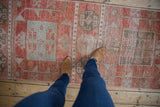 Distressed Oushak runner with faded cinnabar, ivory, and oxidized silver geometric motifs.