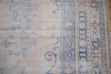 Distressed vintage Oushak rug with faded blue vinery, pale ivory field, and border wear.