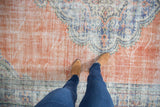Distressed vintage Oushak carpet, featuring worn terracotta field and faded blue patterns.