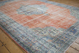 Distressed vintage Oushak carpet showing worn pale terracotta field and blue curvilinear medallion.