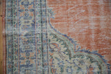 Distressed vintage Oushak rug detail: abrashed terracotta field, geometric blue-ivory spandrel pattern.
