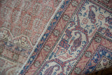 Distressed vintage Sparta carpet close-up, showing pale rust field, indigo border, and fringe.