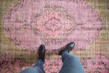 Distressed pink and olive green Oushak carpet, showing faded floral motifs and low pile texture.