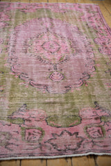 Distressed vintage Oushak carpet, showing faded pink, mauve, olive green, and exposed foundation.