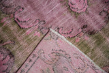 Distressed pink and olive Oushak carpet corner, revealing worn pile, foundation, and fringe.