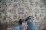 Distressed Oushak carpet with worn silver, sky blue, sandalwood floral pattern below a person's feet.