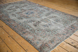 Close-up of distressed Oushak rug with silver, sky blue, and sandalwood floral motifs showing wear.