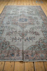 Distressed Oushak rug pile with dusty blue and sandalwood floral patterns.