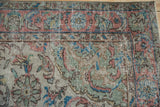 Distressed Oushak rug border with terracotta, blue, green florals, and visible wear.
