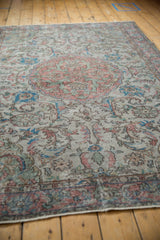 Distressed Oushak rug with dusty terracotta, sky blue floral arabesques, visible foundation.