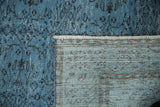 Distressed pale denim blue Oushak rug corner, showing worn pile, fringe, and hand-knotted foundation.