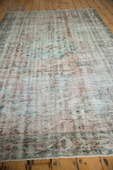 Muted floral motifs and soft wear on the distressed pile of a vintage Oushak rug.