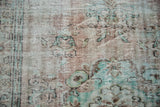 Faded floral motifs and distressed low pile texture on a vintage Oushak rug.
