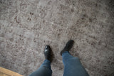 Distressed overdyed Oushak carpet featuring silver and chocolate floral motifs, foundation visible.