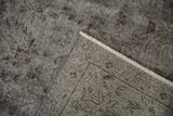Distressed vintage Oushak rug pile with silver-gray tones, chocolate floral motifs, and fringe.