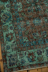 Distressed Oushak carpet corner showing worn sea foam, terracotta floral pattern, and intact selvage.