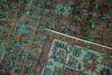 Distressed vintage Oushak carpet showing worn terracotta pile and folded border with sea foam green floral patterns.