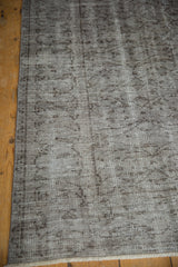 Worn silver and charcoal floral patterns on a distressed Oushak carpet, revealing foundation.
