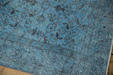 Distressed Oushak carpet's worn dusty blue pile revealing faded floral motifs and foundation.
