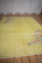 Distressed yellow Oushak carpet corner featuring red and emerald floral motif and even wear.