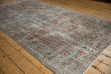 A low angle perspective of a distressed Oushak carpet, highlighting its worn texture and silvery floral design.