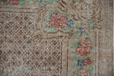 Corner of a distressed Oushak showing a checkered seed design and worn rose bouquet border.