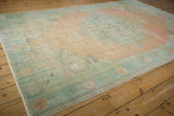 Distressed vintage Oushak rug corner showing wear, with peach and pale sea foam green patterns.