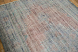 Textured low pile of distressed Oushak rug in dusty blues and muted reds.