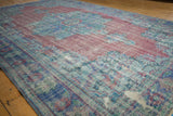 Vintage distressed Oushak rug corner showing faded raspberry, blue motifs, and visible foundation.