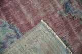 Folded vintage Oushak rug corner showing faded raspberry pile, exposed foundation, and fringe.