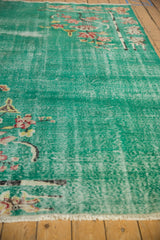 Distressed green Art Deco carpet's worn pile, showing lotus flowers and visible foundation.