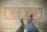 Distressed vintage Oushak rug displaying a pale burnt orange medallion with diamond and pinwheel florals.