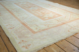 Oushak rug corner with pale burnt orange banded border and distressed ivory floral patterns.