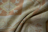 Soft, distressed Oushak rug pile with pale burnt orange and ivory pinwheel floral motifs.