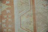Distressed Oushak rug close-up showing worn pale orange and ivory pile with faded arrowed patterns.