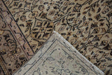 Corner view of a distressed Sparta carpet, showing muted scrolling vinery, visible foundation, and fringe.