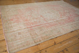 Distressed Oushak carpet corner, faded pale rose, ivory, seafoam green, and fringed selvage.