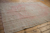 Distressed vintage Oushak carpet corner with worn pale rose and ivory hues, intact selvage.