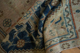 Folded section showing distressed indigo blue geometric border and worn beige pile.