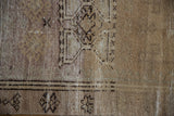 Distressed Oushak rug pile texture showing wear, visible foundation, faded sand, and geometric motifs.