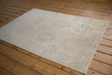 Distressed Oushak rug with soft ivory pile and muted pink, blue floral details.
