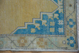 Distressed gold Oushak rug corner with worn pile and sky blue floral border detail.