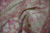 Distressed pile showing pinwheel floral motifs in pale aubergine and ivory on the Oushak rug.
