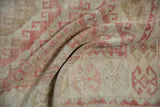 Distressed Oushak rug pile with dusty raspberry and beige geometric hook and latch pattern.