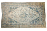 Distressed vintage Oushak carpet with ivory field, slate blue medallion, and floral motifs.
