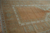 Distressed Oushak rug showing copper field, pale sea foam geometric palmette and running-t borders.
