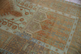 Distressed Oushak rug detail: pale sea foam reciprocating border and plant motifs on terracotta.